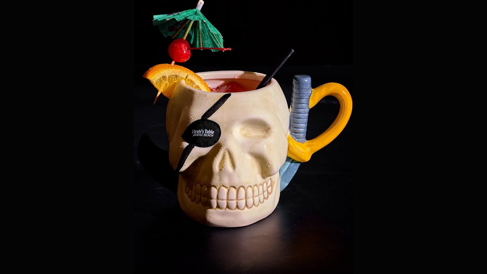 A skull-shaped pirate mug cocktail with an orange slice and cherry at Pirate's Table